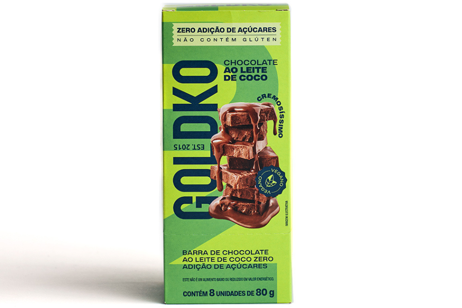 Embalagem do chocolate GoldKo ao leite de coco com zero adição de açúcares, vegano e sem glúten, contendo imagem de pedaços de chocolate cremoso empilhados e texto destacando os benefícios do produto.